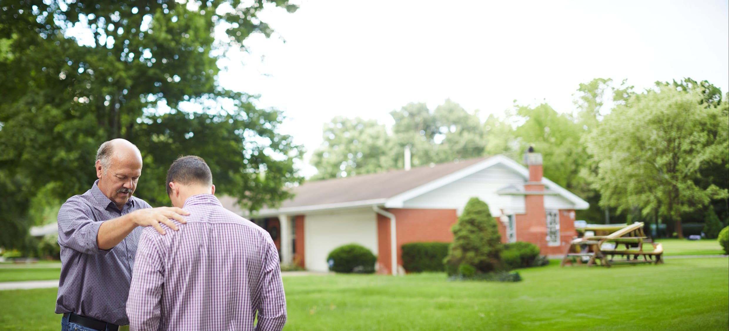 A pastor praying with a hand on a young church planter's shoulder outside a church
