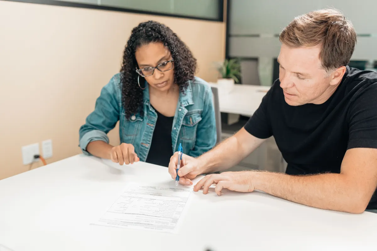 Two people signing a printed agreement across a table